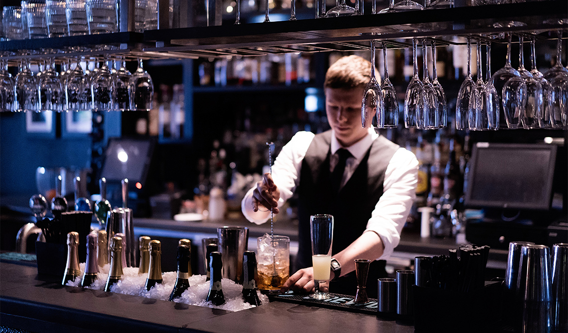 Barman à l'arrière de son bar en train de réaliser un cocktail